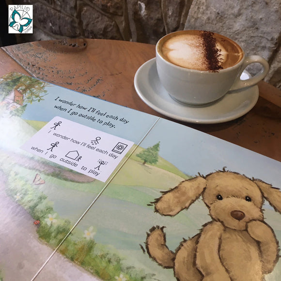 Photo of a double page spread of a Jellycat kids story book. Underneath the wording a makaton translation can be seen. A cappuccino is seen behind the book.