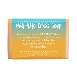 Photo of the Dandelion Stationery Mid-Life Crisis Soap. The label is orange and turquoise ombre. The caption on the soap packaging says: 'Mid-Life Crisis Soap. An aromatic scent of fast cars and motorcycles mixed with subtle notes of a fancy new hobby. The occasional hint of a tattoo or piercing.'