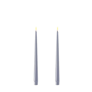Photo of 2 Dust Blue 28cm tapered dinner candles. Their led flames are lit and they have black wicks.