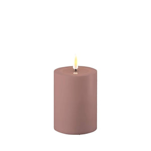 Photo of a Deluxe HomeArt dust red outdoor LED Pillar candle that is 7.5cm wide and 10cm tall. Although the colour is called dust red the colour in real life is more of a light lilac. At the top of the candle is a clear resign pool that looks like a pool of melted wax. The flame is white and orange and is on a black wick.