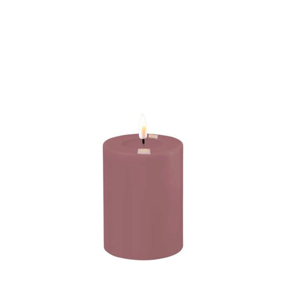Photo of a Deluxe HomeArt Light Purple LED Pillar candle that is 7.5cm wide and 10cm tall. At the top of the candle is a clear resign pool that looks like a pool of melted wax. The flame is white and orange and is on a black wick.