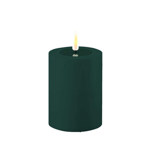 Photo of a Deluxe HomeArt Dark green outdoor LED Pillar candle that is 7.5cm wide and 12.5cm tall. At the top of the candle is a clear resign pool that looks like a pool of melted wax. The flame is white and orange and is on a black wick.