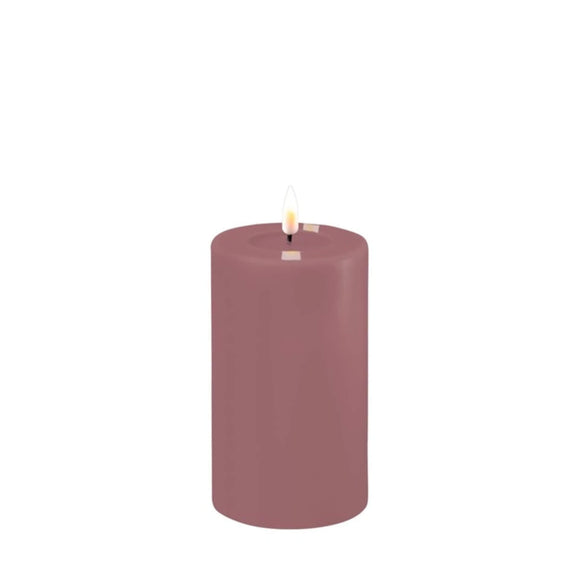 Photo of a Deluxe HomeArt Light Purple LED Pillar candle that is 7.5cm wide and 12.5cm tall. At the top of the candle is a clear resign pool that looks like a pool of melted wax. The flame is white and orange and is on a black wick