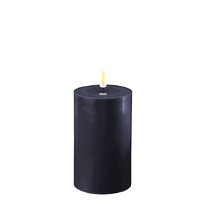 Photo of a Deluxe HomeArt Royal Blue LED Pillar candle that is 7.5cm wide and 12.5cm tall. At the top of the candle is a clear resign pool that looks like a pool of melted wax. The flame is white and orange and is on a black wick.