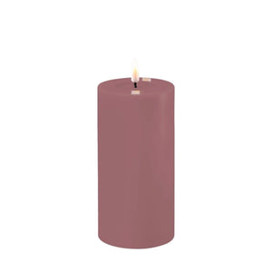 Photo of a Deluxe HomeArt Light Purple LED Pillar candle that is 7.5cm wide and 15cm tall. At the top of the candle is a clear resign pool that looks like a pool of melted wax. The flame is white and orange and is on a black wick.