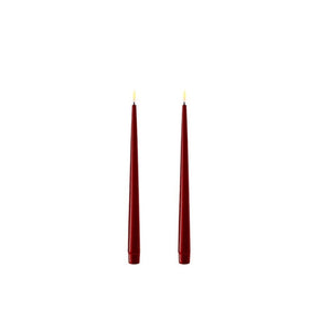 Photo of 2 bourgogne red (deep burgundy) 28cm tapered dinner candles. Their led flames are lit and they have black wicks.