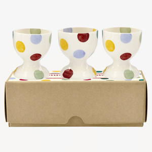 Photo of a cardboard box with 3 handmade, pottery egg cups sitting on it. Emma Bridgewater polka dots are shades of red, blue, yellow and green.