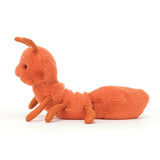 Side view of the Wriggidig Ant cuddly toy from Jellycat. It is completely orange apart from its black eyes and smile. It has 6 legs and 2 antenna. 