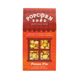 Photo of the Popcorn Shed of Pecan Pie Popcorn. The box is shaped like a shed and is in dark shades of orange. Through the window the popcorn can be seen. The words on the box say 'Handcrafted Gourmet Popcorn. Gluten Free. All natural ingredients. Pecan Pie. Caramel Popcorn with Pecan Nut Pieces. 80g.'