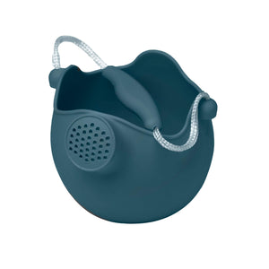 Photo of the Scrunch Watering Can in French Navy. This silicone watering can is shaped like a sphere, with the top taken off in a wavy way. A spout slightly protrudes just below the edge on one side. The handle is made from rope with a bit of matching silicone at the top for easier holding.